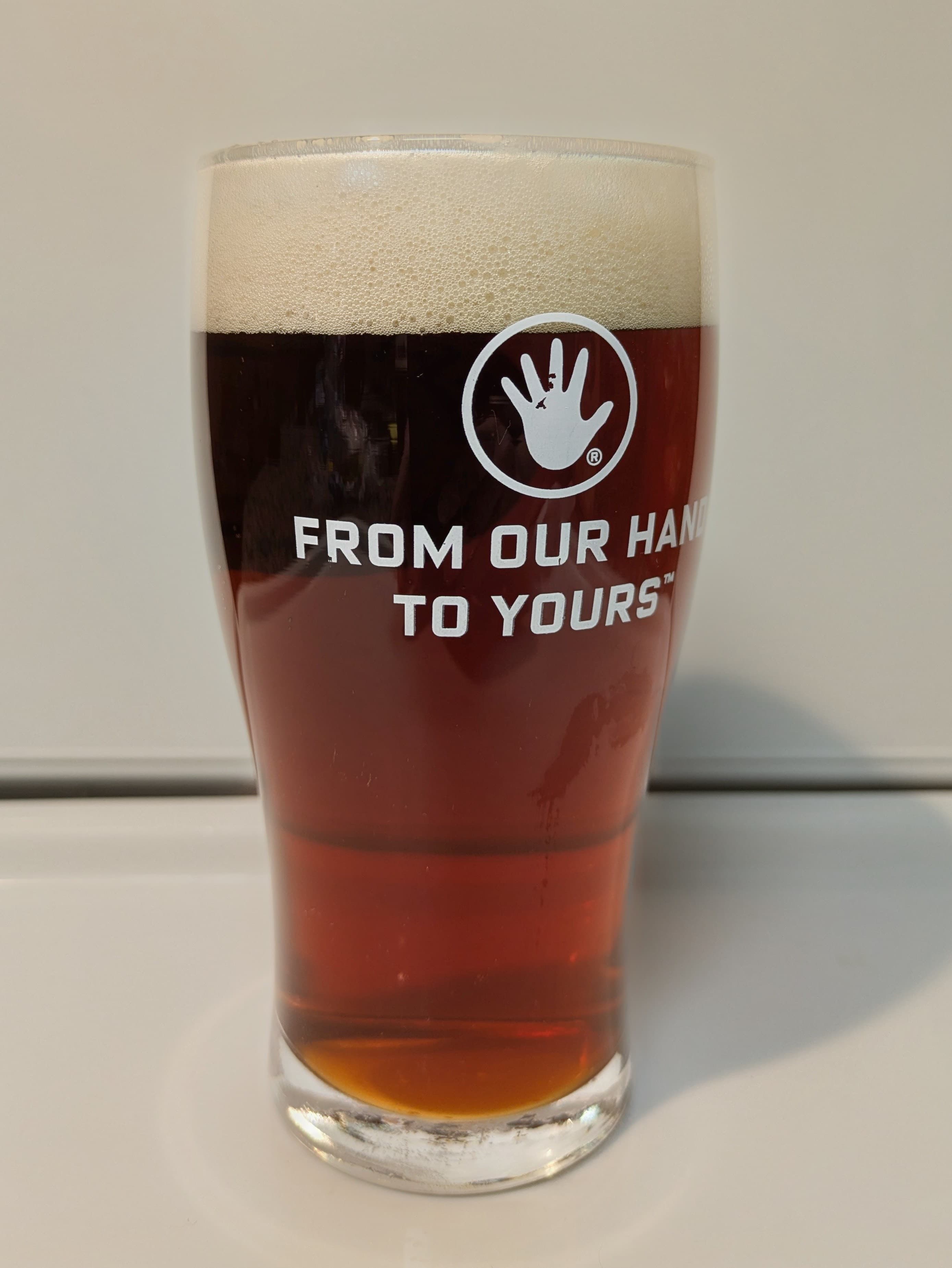 Amber colored clear beer in a glass that reads from our hands to yours