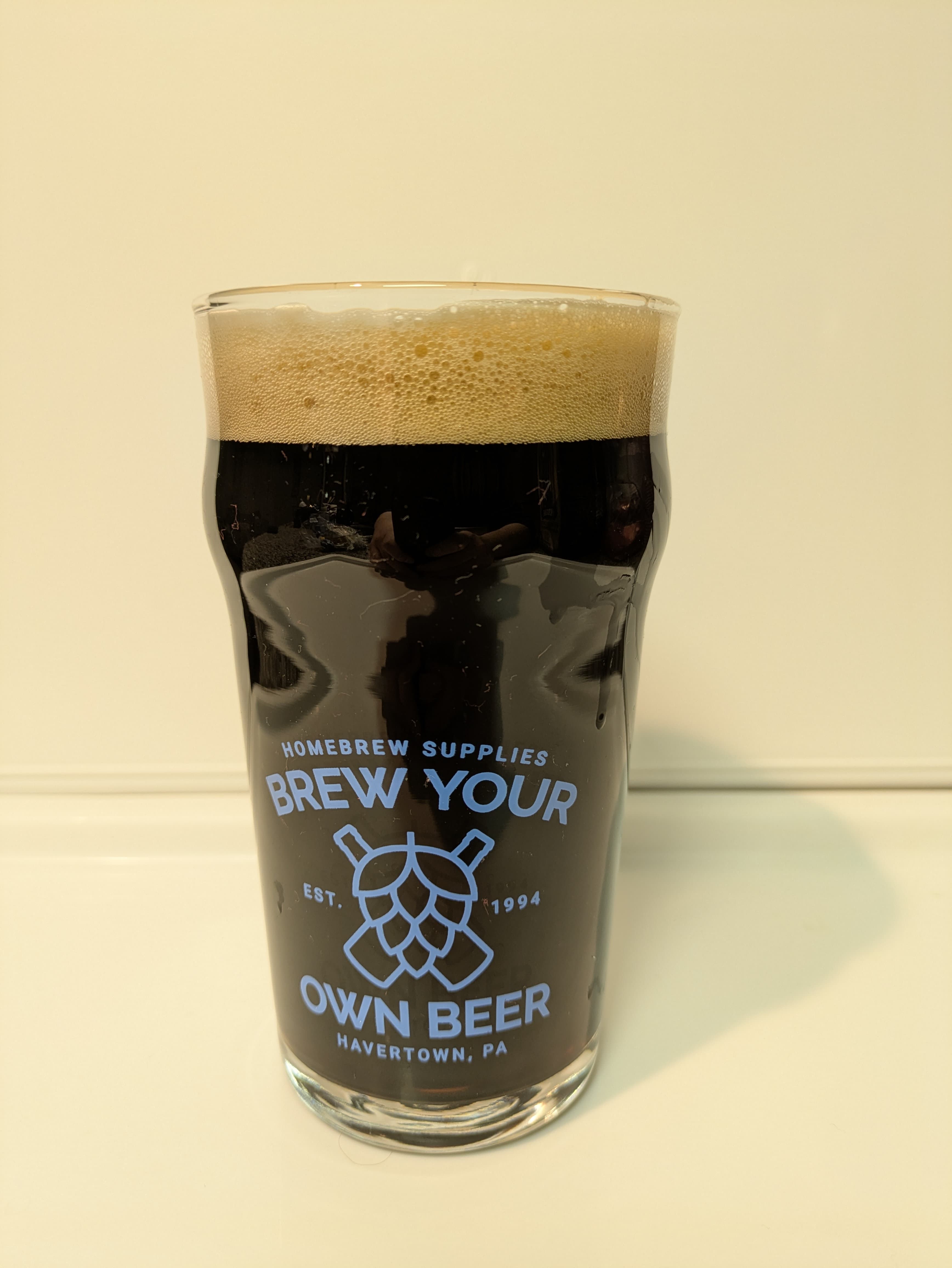 Pitch-black beer in a glass that reads brew your own beer